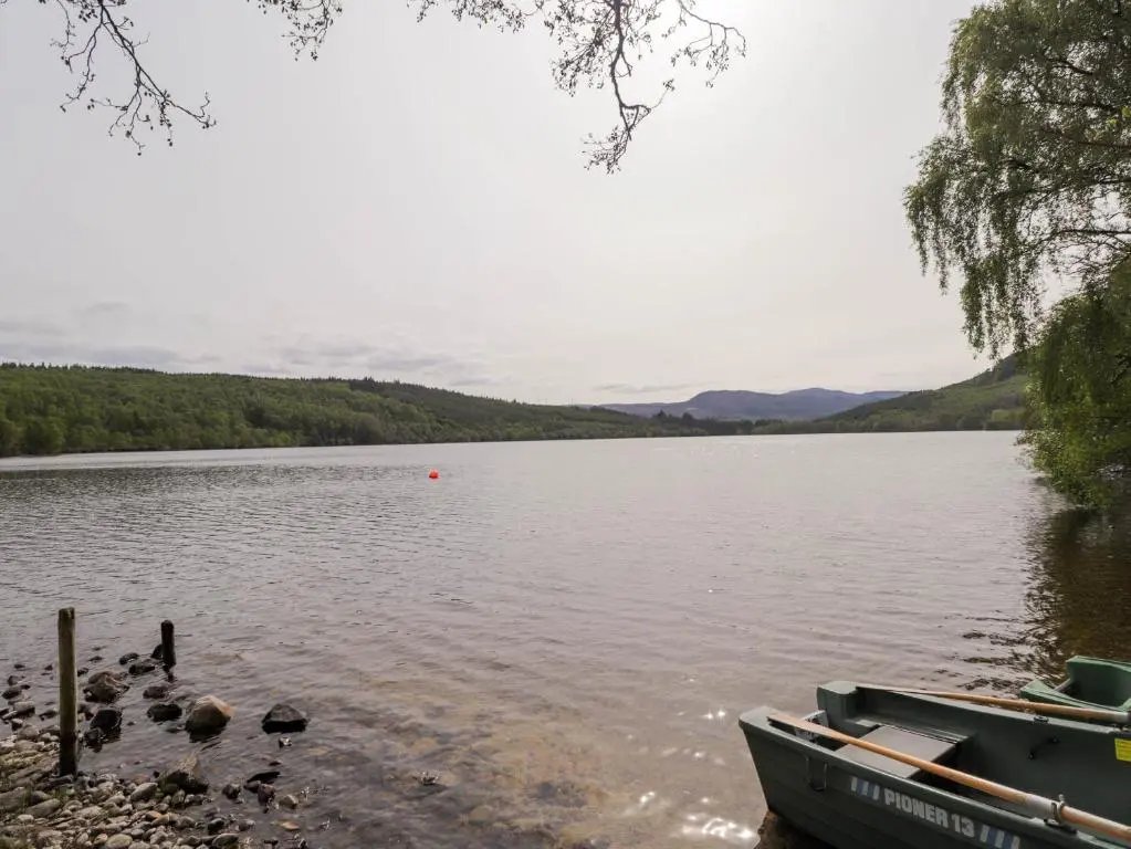a boat sitting on the shore of a lake at Pebbles Cottage in Contin