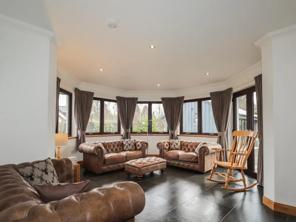 a living room with couches and chairs and windows at Little Chestnut in Muir of Ord