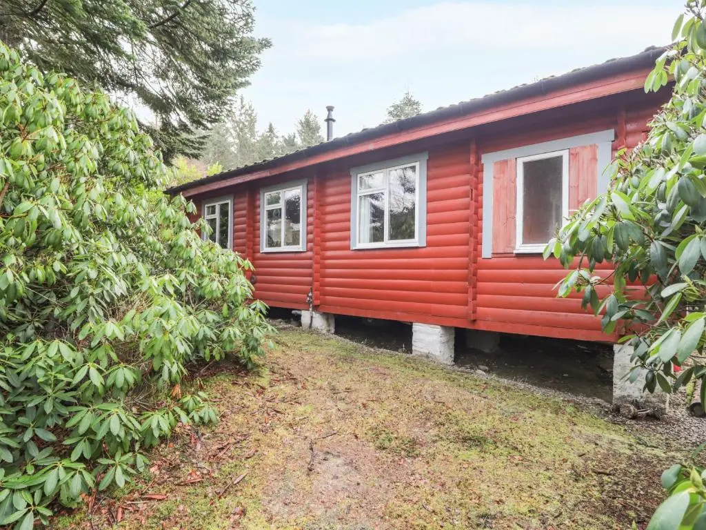 a red cabin with white windows in a forest at Rowan Lodge in Strathpeffer