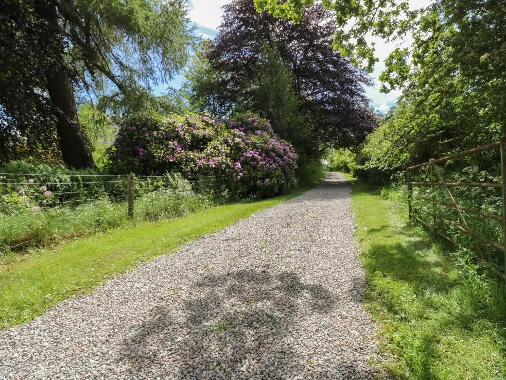a gravel road with trees and flowers on it at The West Wing in Skye of Curr