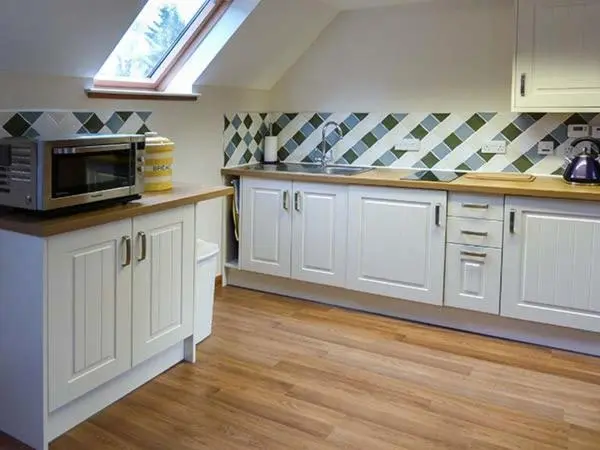 a kitchen with white cabinets and a microwave oven at Lakefield Apartment in Bearnock