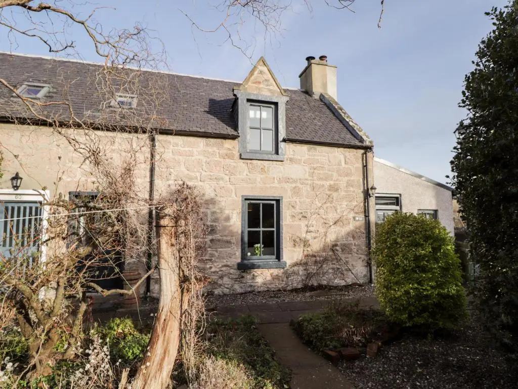 an old stone house with a window and bushes at 59 Society Street in Nairn
