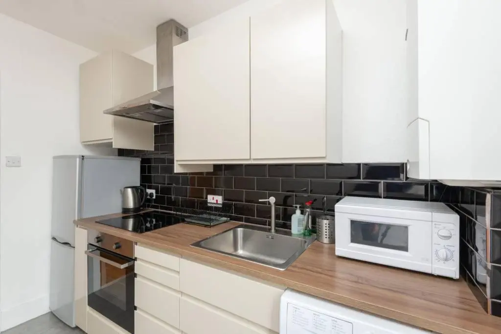 a kitchen with white cabinets and a sink and a microwave at Ness Central Apartment - Greig Street in Inverness