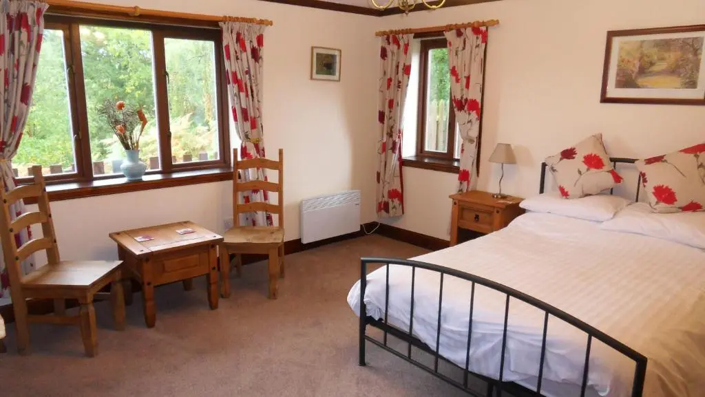 a bedroom with a bed and a table and chairs at Meadowside Cottages in Balavil