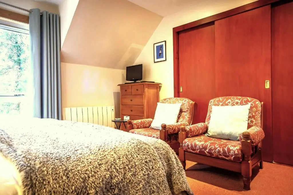 a bedroom with two chairs and a bed and a tv at Crubenbeg Country House in Newtonmore