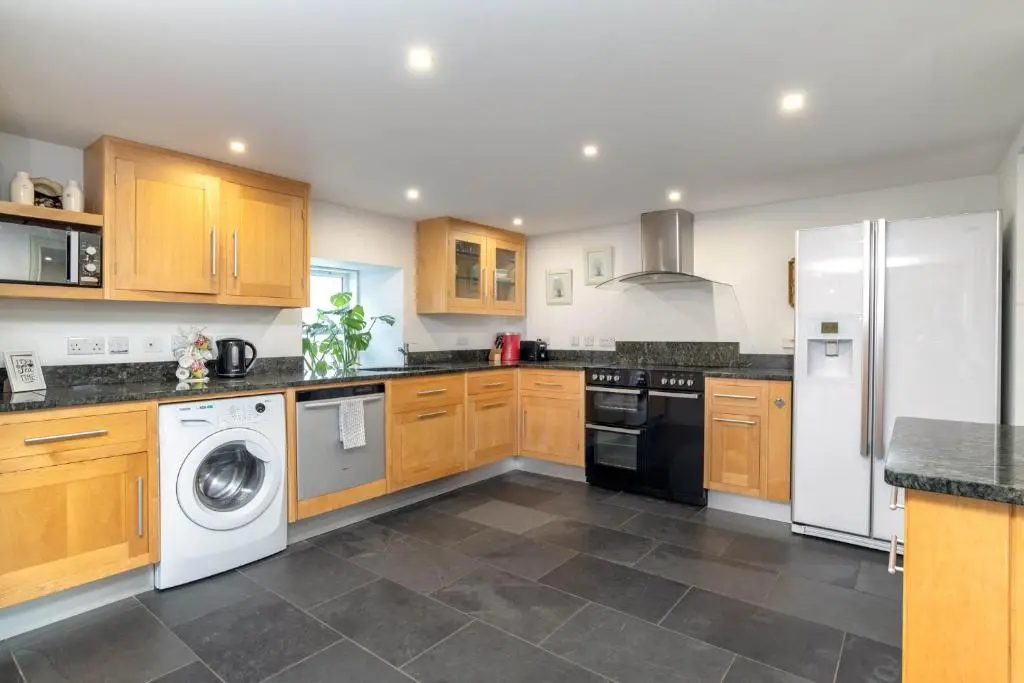 a kitchen with wooden cabinets and a washer and dryer at Riverside Cottage with wood fired hot tub in Cairngorms in Ballater