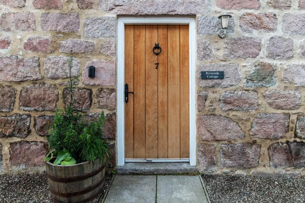 a wooden door in a stone building with a potted plant at Riverside Cottage with wood fired hot tub in Cairngorms in Ballater