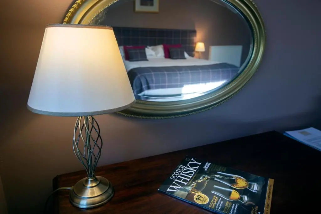 a lamp on a table with a book and a mirror at Cardhu Country House in Aberlour