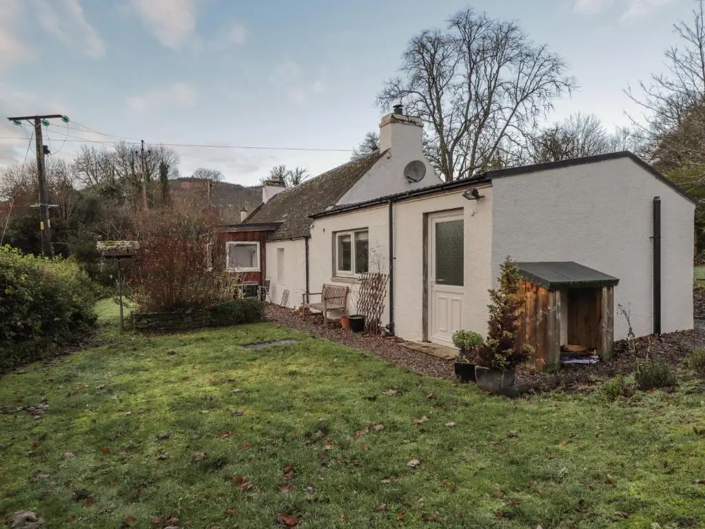 a white house with a yard in front of it at Lilac Cottage in Strathpeffer