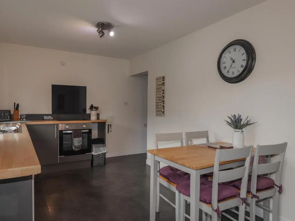 a kitchen with a table and a clock on the wall at Lilac Cottage in Strathpeffer