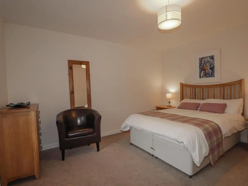 a bedroom with a bed and a chair at Lilac Cottage in Strathpeffer