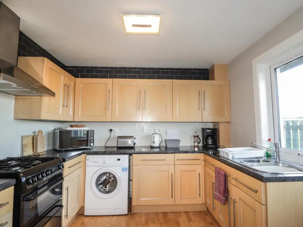a kitchen with wooden cabinets and a washer and dryer at Rose Cottage in Lybster