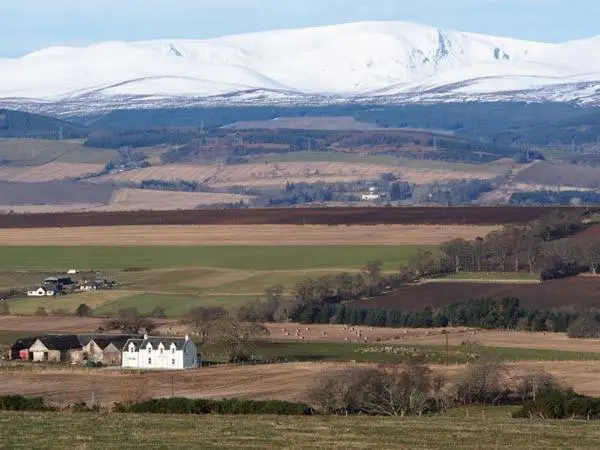 a large white house in a field with snow covered mountains at Pine Lodge in Resolis