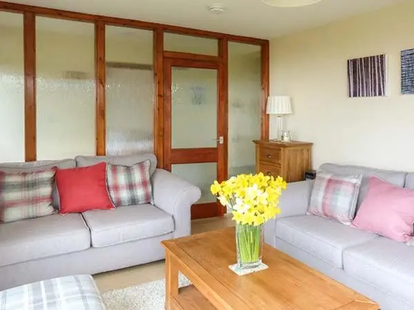 a living room with couches and a vase of flowers on a table at Pine Lodge in Resolis