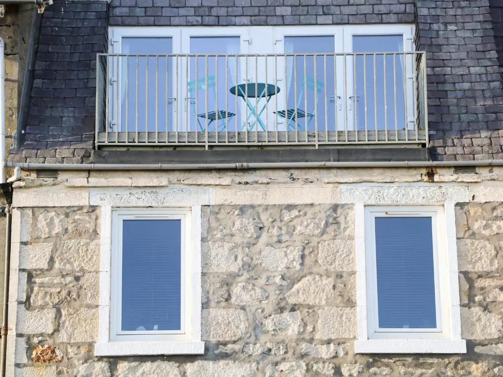a stone building with a balcony and two windows at Seascape in Lossiemouth