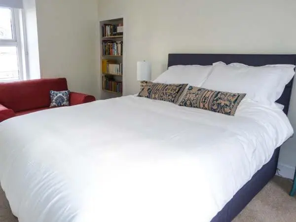 a large white bed in a bedroom with a red chair at Grace Cottage in Buckie