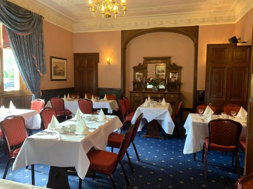 a restaurant with white tables and chairs and a chandelier at Ramnee Hotel in Forres