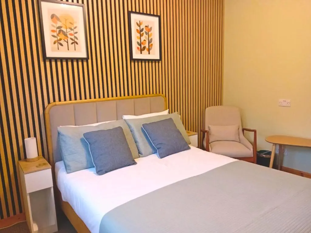 a bedroom with a bed with blue pillows and a chair at Deveron Lodge B&B in Turriff