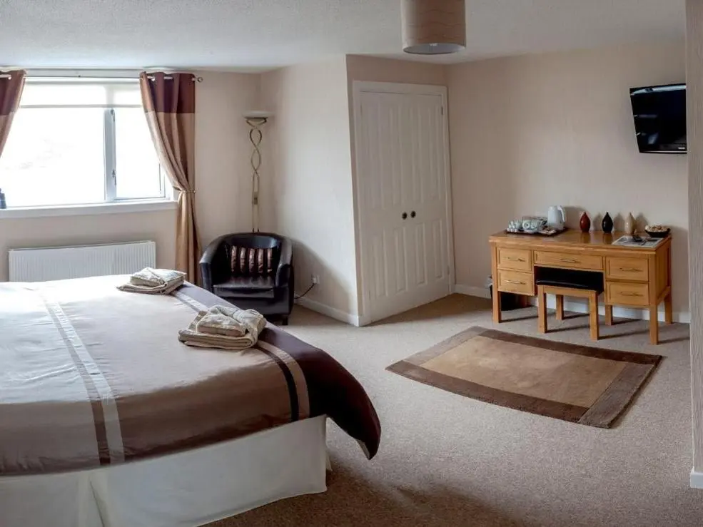 a bedroom with a bed and a desk and a window at Ardlair Guest House in Ullapool