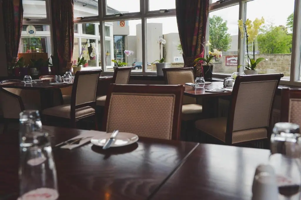 a dining room with tables and chairs and windows at Sunninghill Hotel in Elgin