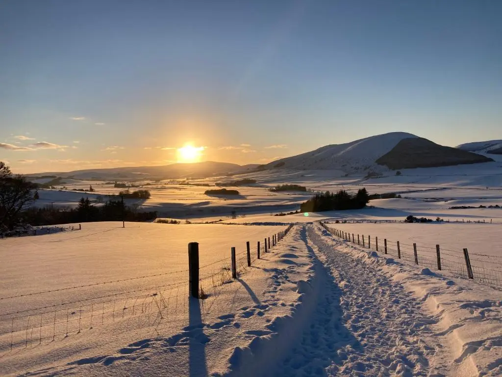 a fence in a snow covered field with the sunset at Woodside Steading in Huntly