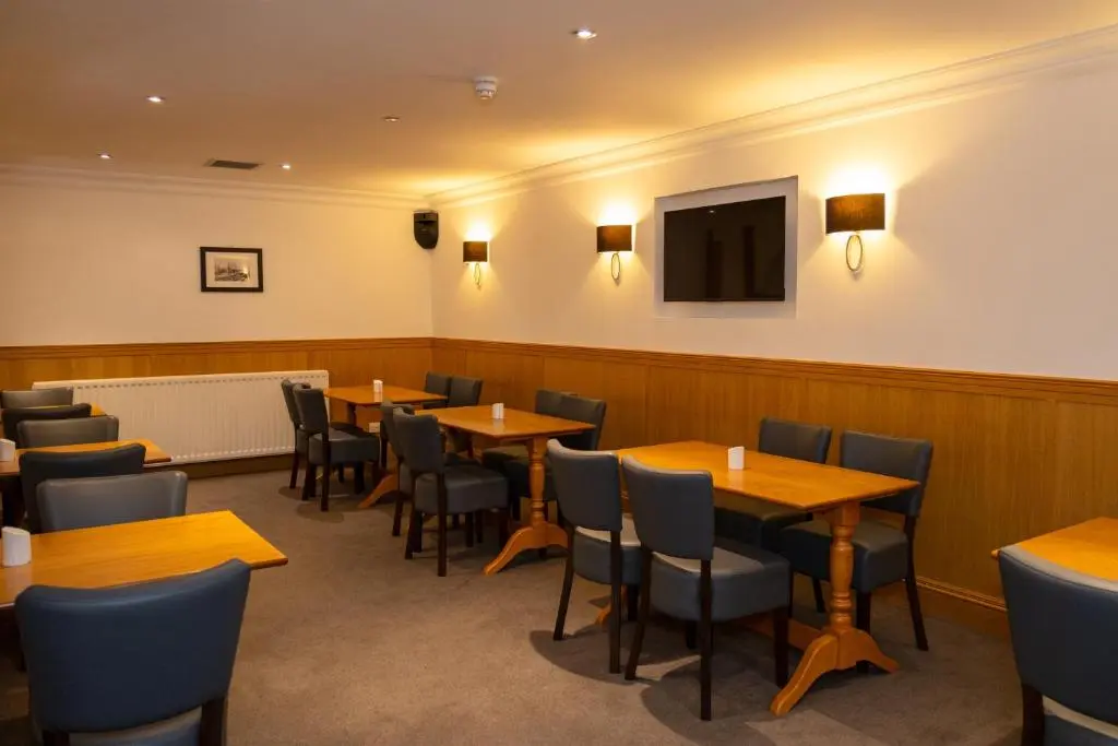 a restaurant with wooden tables and chairs and a flat screen tv at Station Hotel in Ellon