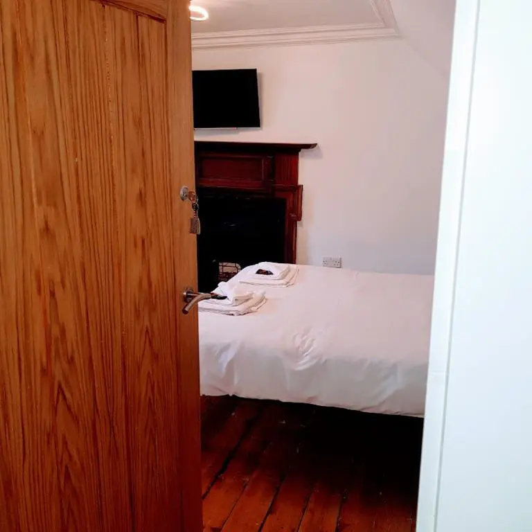 a bedroom with a bed with white sheets and a television at Ness City Cottage in Inverness