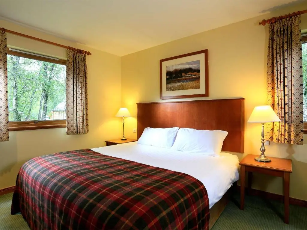 a hotel room with a large bed and two windows at Macdonald Woodland Lodges at Macdonald Aviemore Resort in Aviemore