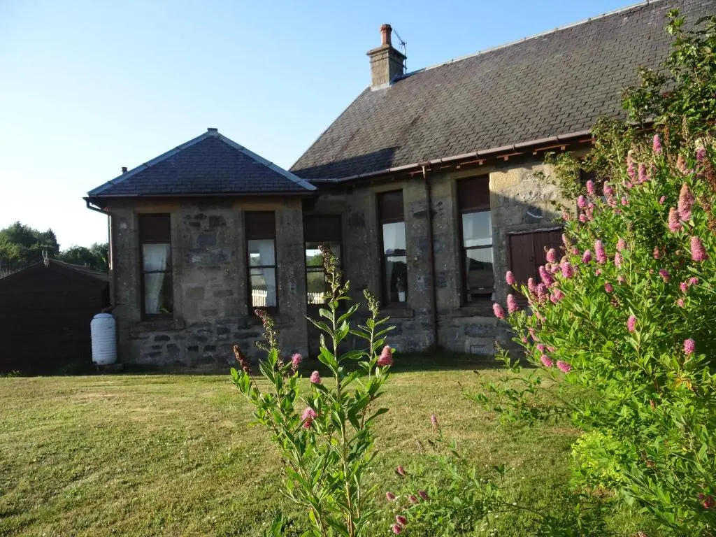 an old stone house with pink flowers in the yard at Shetland Cottage Kincraig in Kincraig