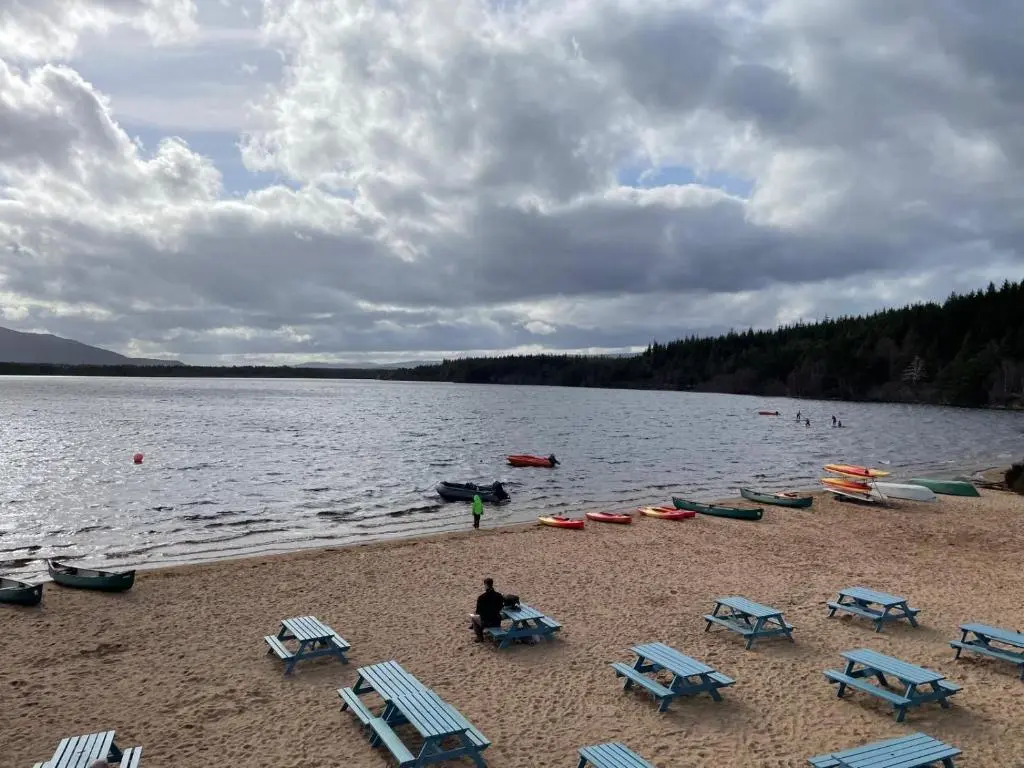 a group of chairs and tables on a beach with a lake at Shetland Cottage Kincraig in Kincraig