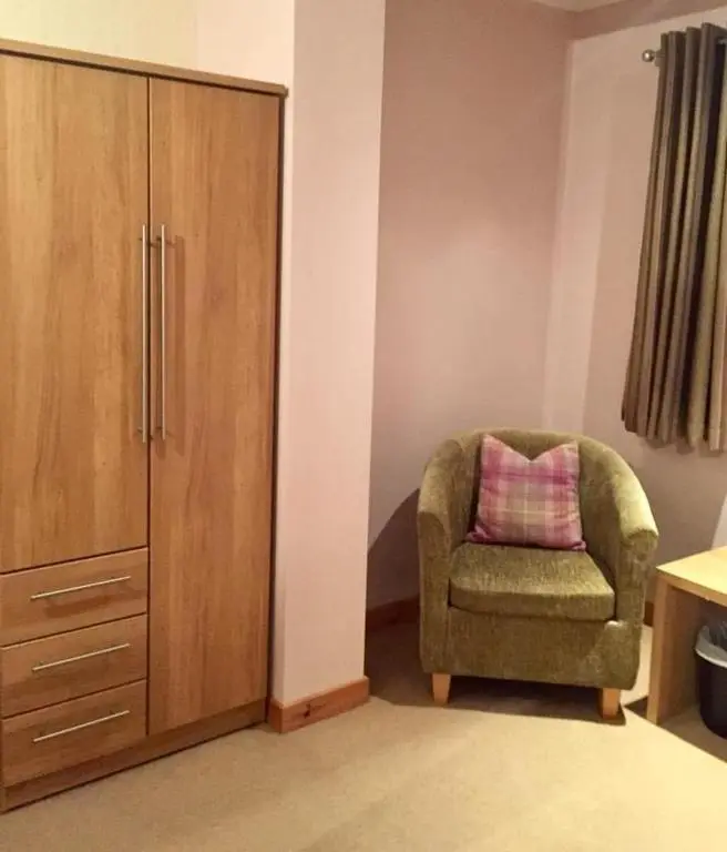 a green chair with a pink pillow sitting next to a cabinet at Island View Guest House in Ullapool