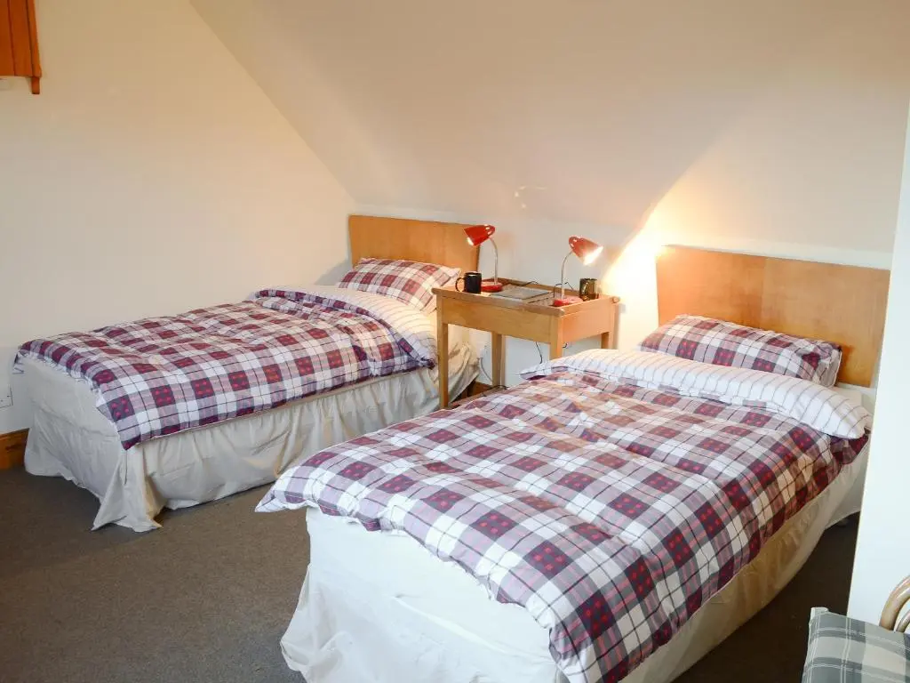 a bedroom with two beds and a table with a lamp at Lower Brae in Achnahanat