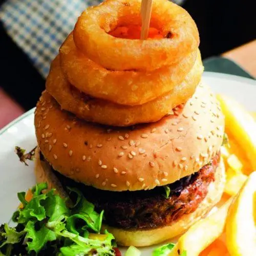 a hamburger with onion rings on top on a plate at The Royal Oak Hotel in Cullen