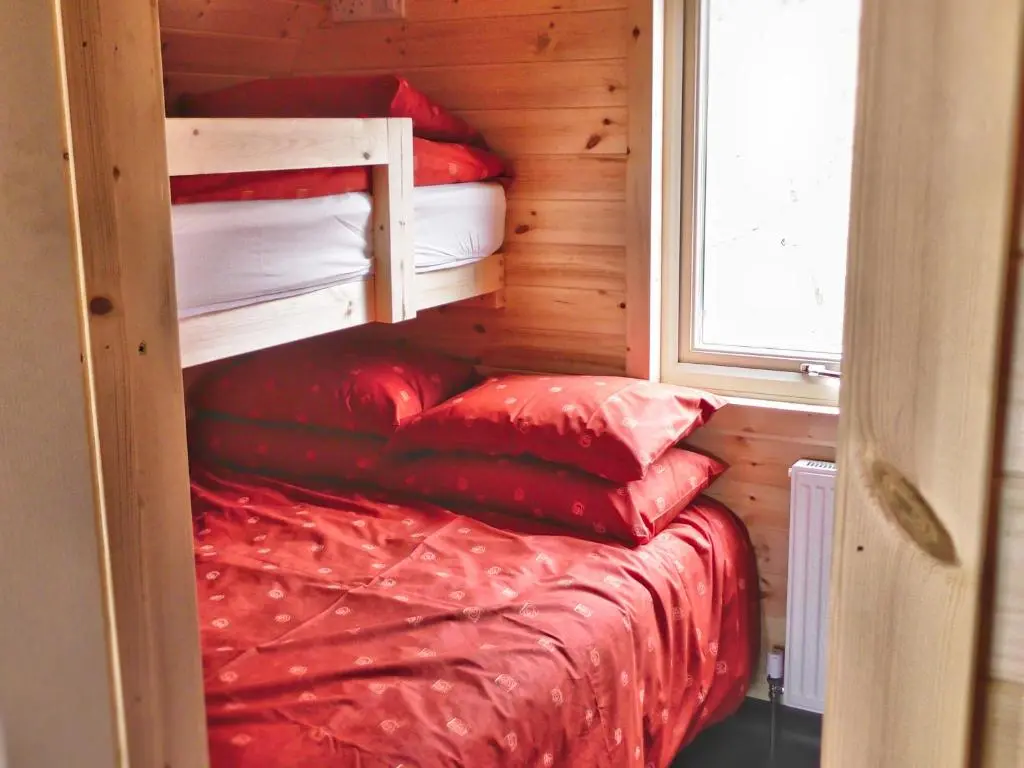 a small room with a bed with red sheets and pillows at Tigh an Each B&B & Laggan Glamping in Newtonmore