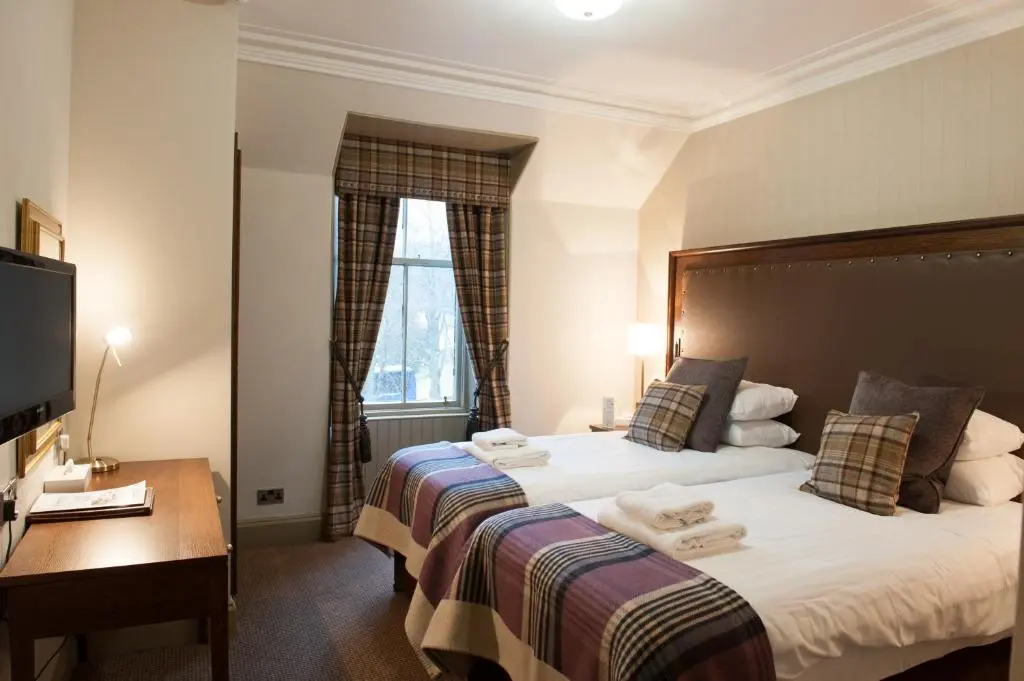 a bedroom with two beds and a desk and a window at Cairngorm Hotel in Aviemore