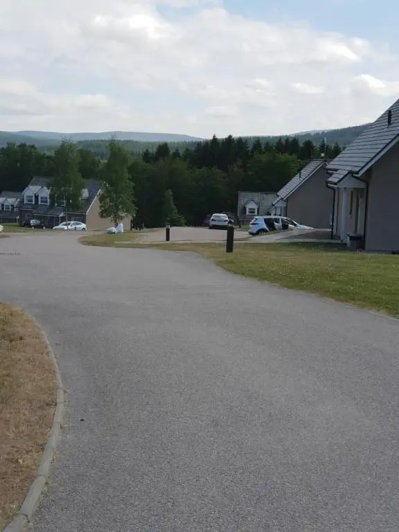 an empty street in a residential neighborhood with cars parked at Inchmarlo villa27 in Banchory