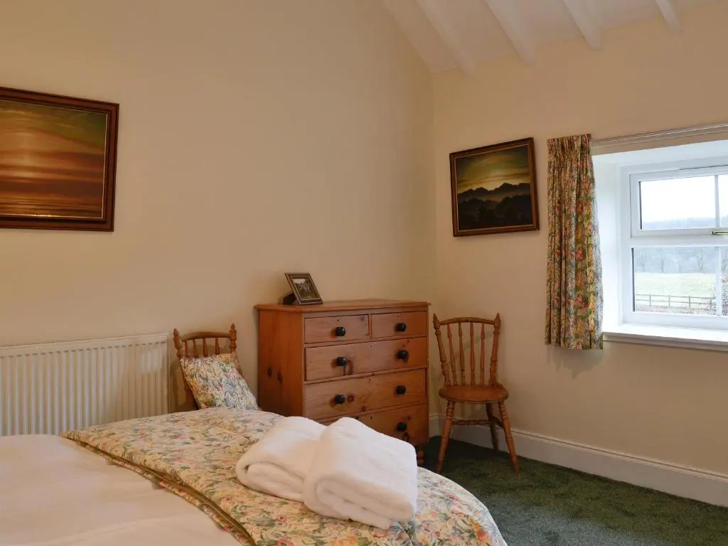 a bedroom with a bed and a dresser and a window at Inverchroskie Cottage in Enochdhu