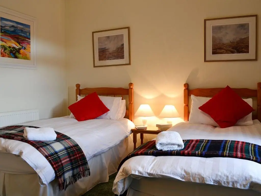 a bedroom with two beds with red pillows at Inverchroskie Cottage in Enochdhu