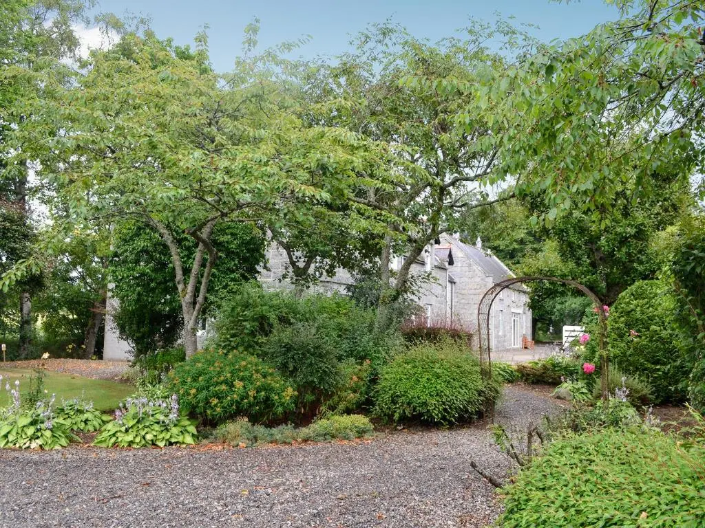 a garden with a greenhouse and some bushes and trees at The Coach House in Alford