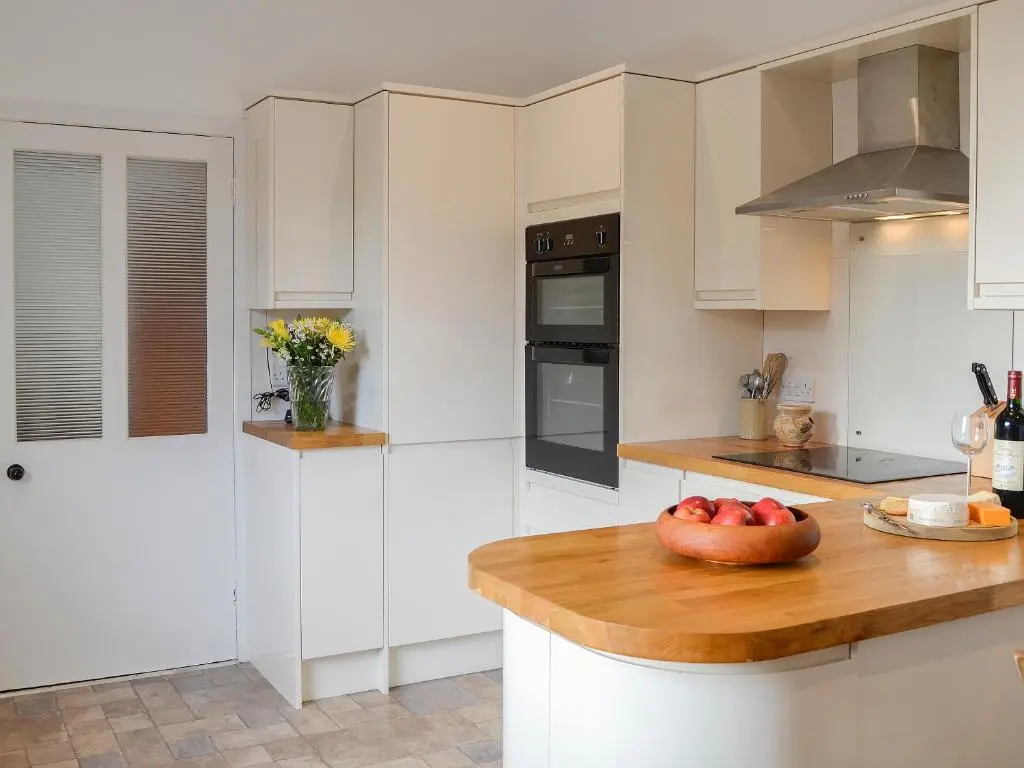 a kitchen with white cabinets and a bowl of fruit on a counter at The Coach House in Alford