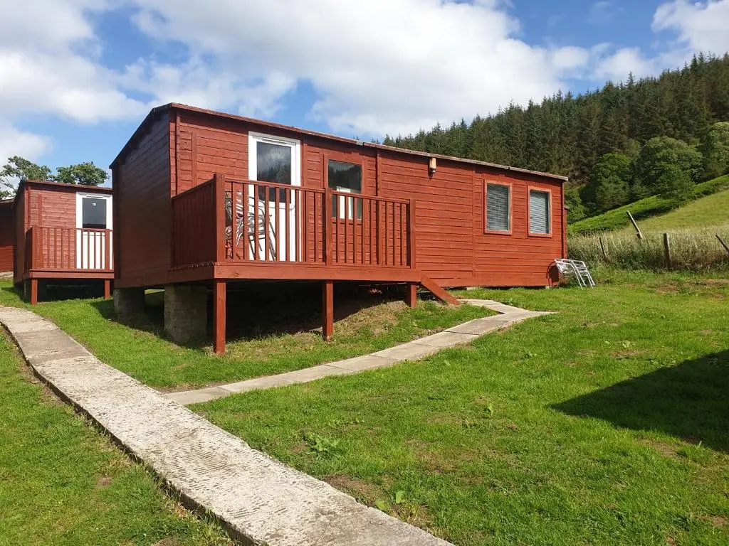 a wooden house with a deck on a grass field at Clunebeg Lodge in Drumnadrochit