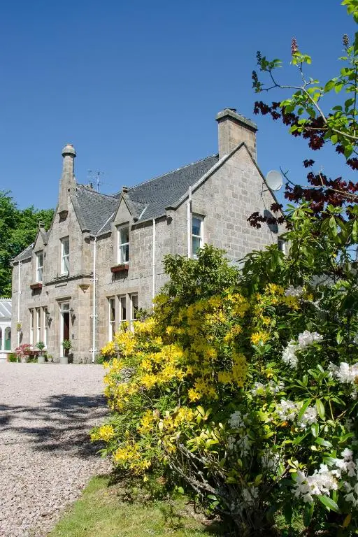 an old stone house with flowers in front of it at Ravenscourt House, Guest House in Grantown on Spey