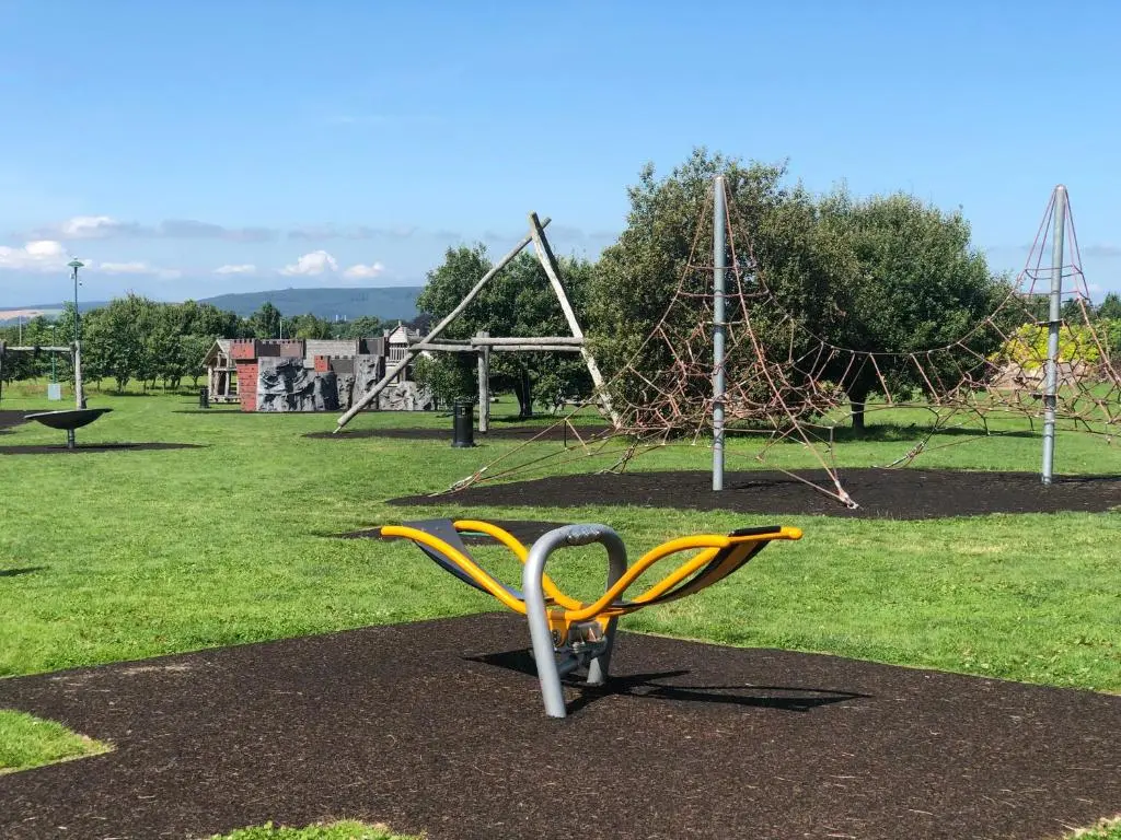 a yellow bench in a park with a playground at One-Bedroom Apartment - Wyvis Free Parking in Inverness