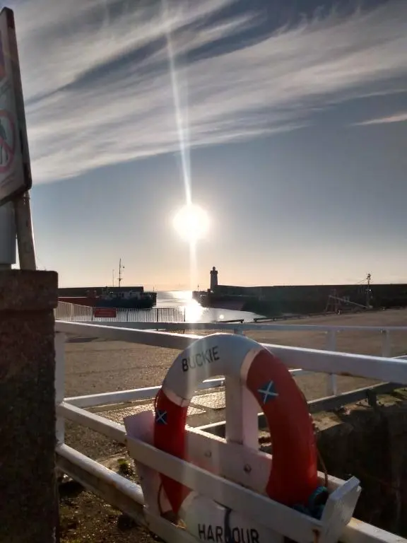 a life preserver sitting on a fence with a lighthouse in the background at Marine Hotel in Buckie