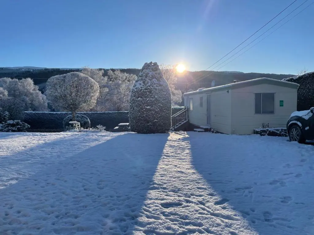 a driveway covered in snow with the sun behind a house at Forest View - Adults Only - Maximum 2 Guests in Drumnadrochit