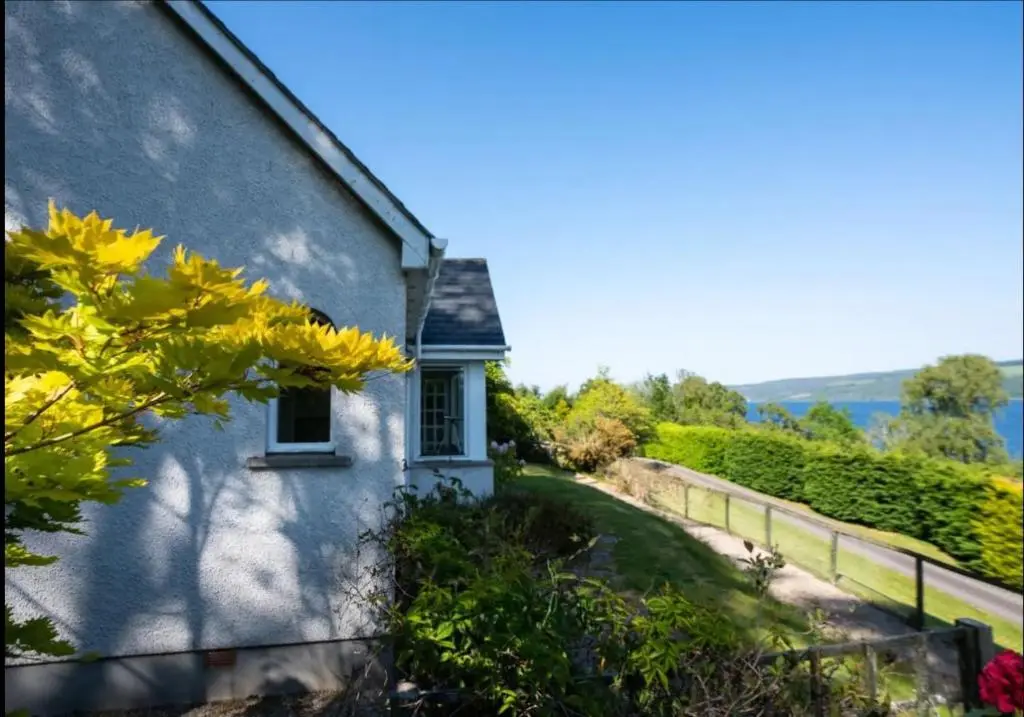 a white building with a window and a fence at Loch Ness Cottages in Brackla