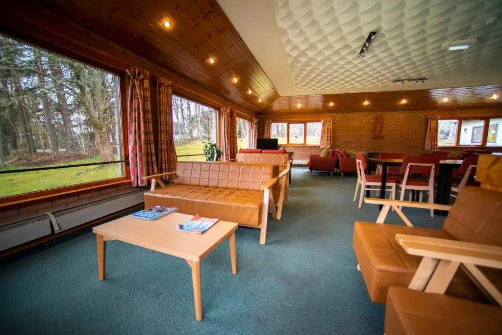 a living room with couches and tables and windows at Aviemore Youth Hostel in Aviemore