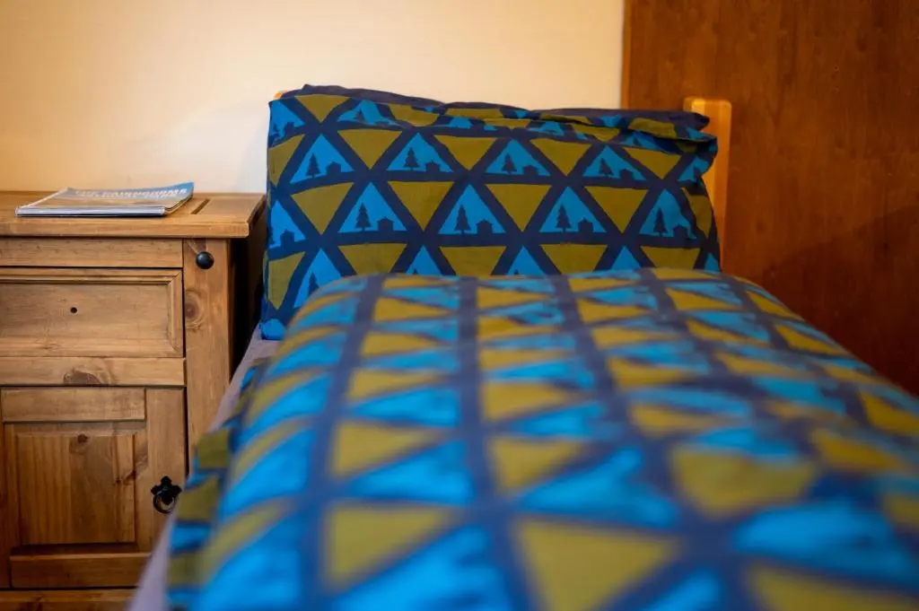 a bed with a blue and yellow comforter and a wooden cabinet at Aviemore Youth Hostel in Aviemore