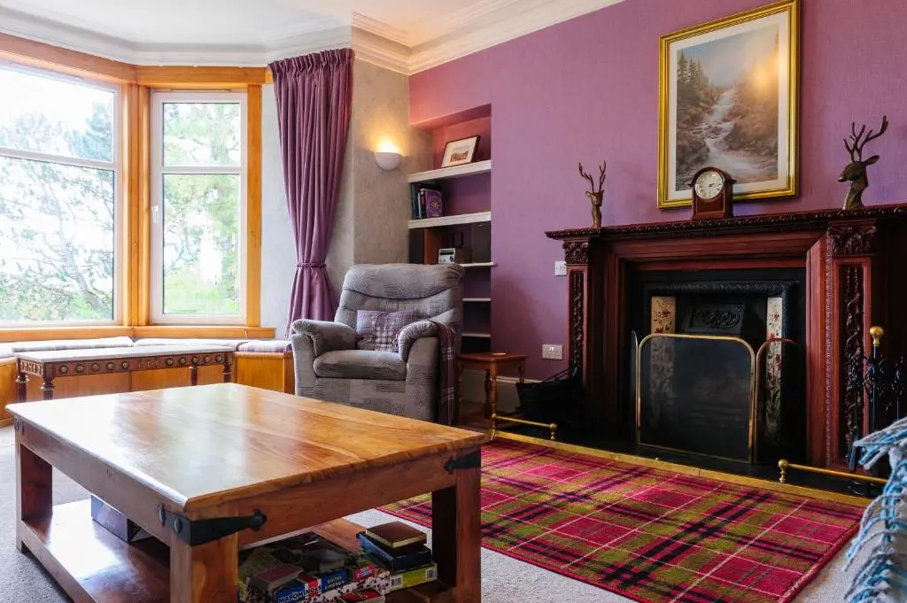a living room with a table and a fireplace at Alvey House in Newtonmore