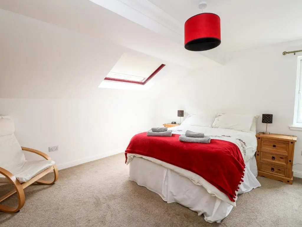 a bedroom with a bed with a red blanket and a chair at Tigh Na Drochit in Garve